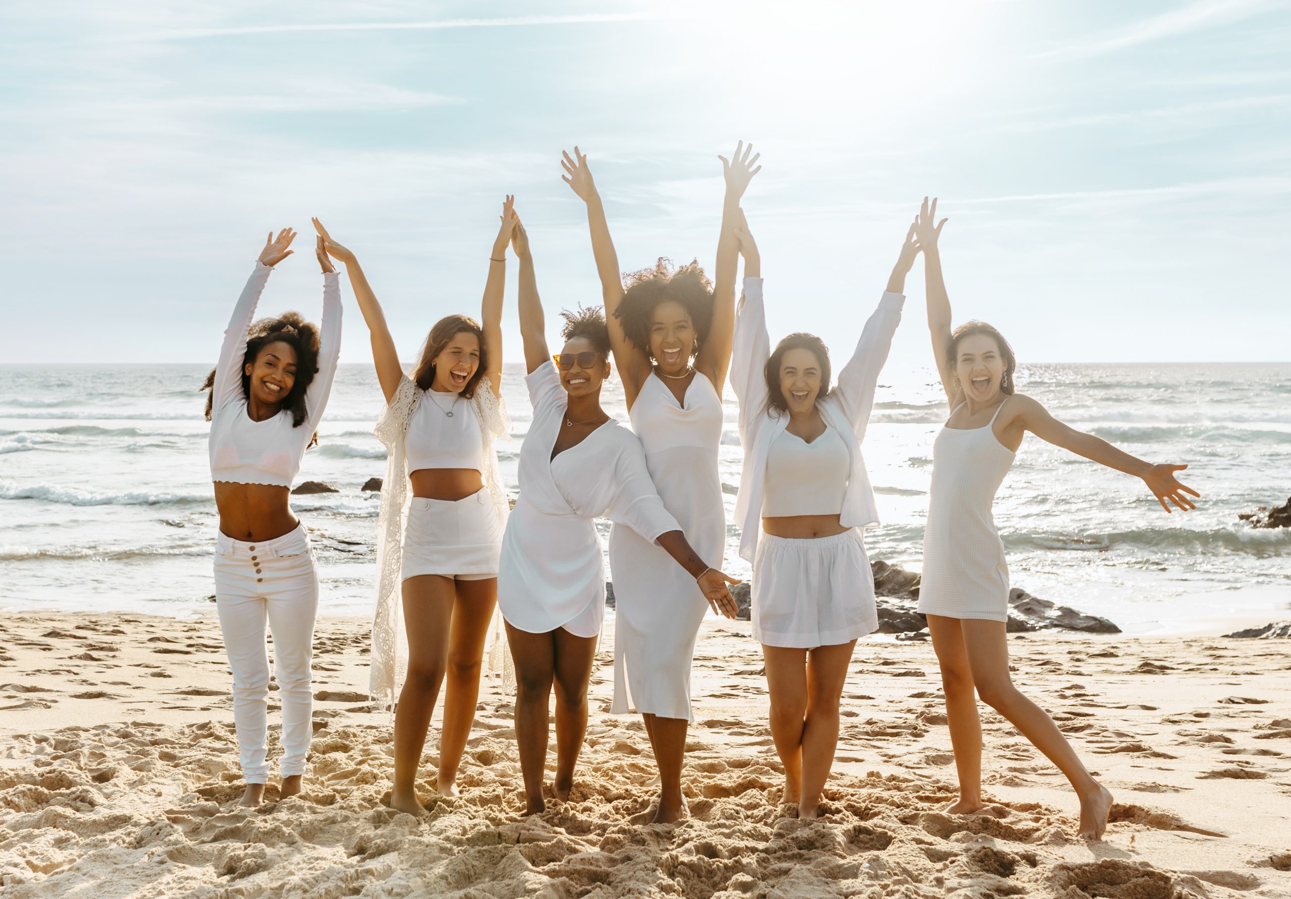 Joyful multiracial women with hands up posing on the beach, having fun and dancing, enjoying hen party outdoors